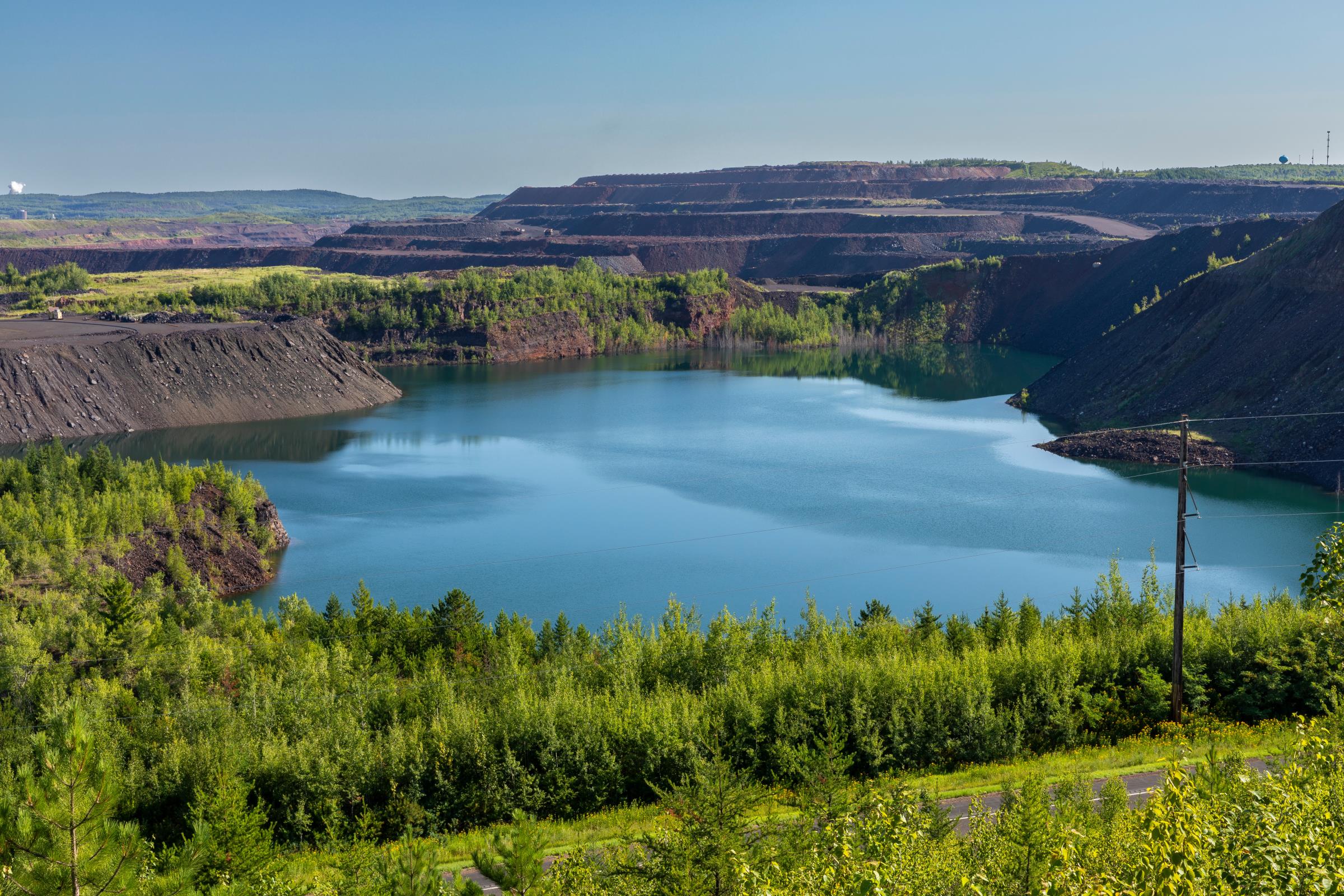 An aerial view of an iron ore mine landscape on a sunny day that features a bright blue lake in the mine pit