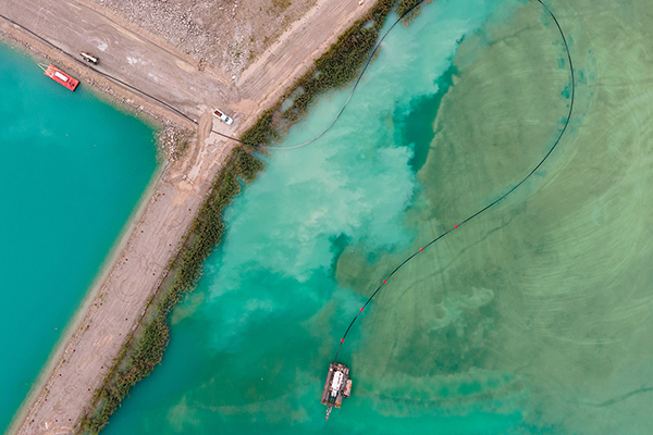 Aerial drone view of colorful turquoise blue mining tailings with vehicles and boat