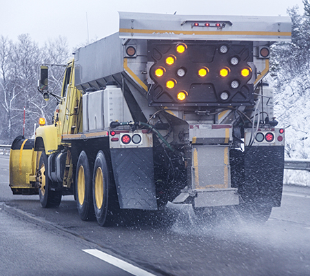 A snowplow scatters road salt on a highway during winter. Road salt—typically sodium chloride—helps keep winter roads, sidewalks, and parking lots safe, but it can also enter the environment during storage, transport, or application.