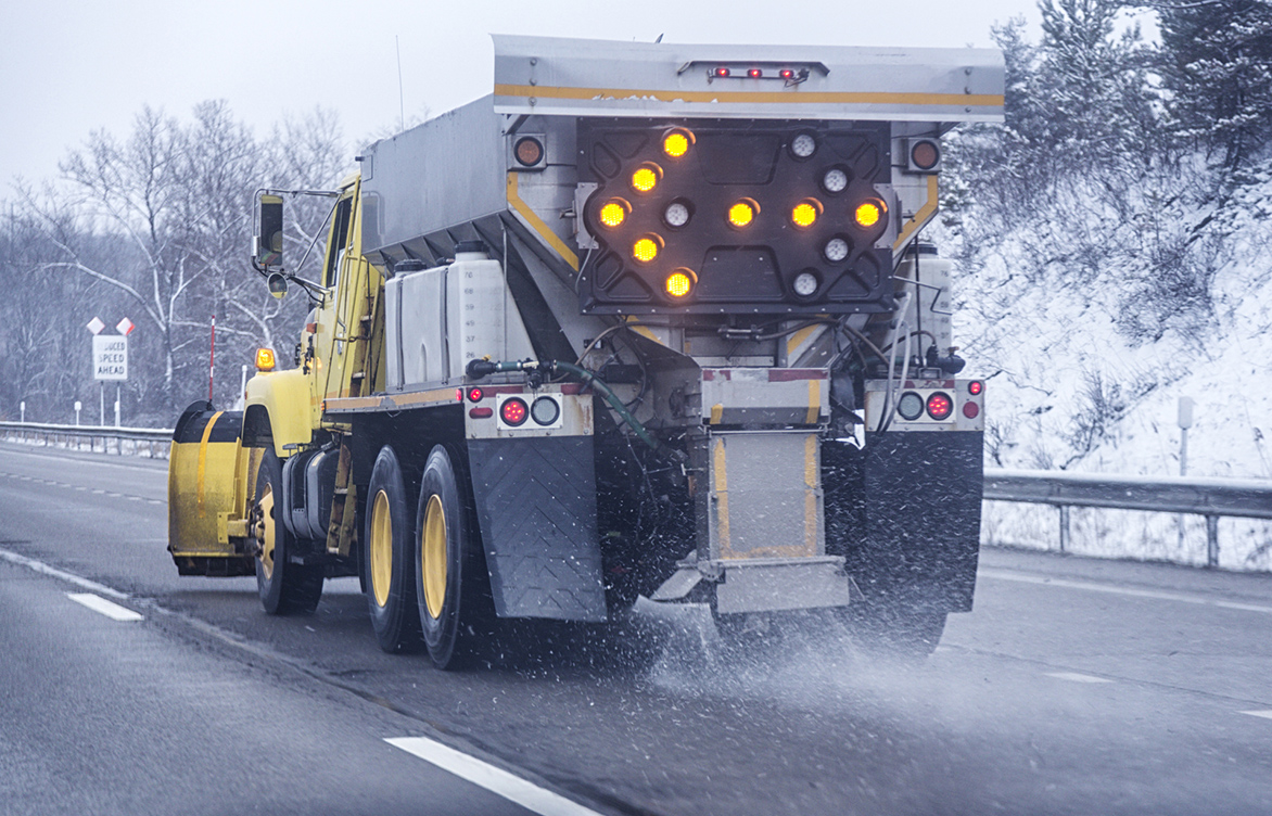 A snowplow scatters road salt on a highway during winter. Road salt—typically sodium chloride—helps keep winter roads, sidewalks, and parking lots safe, but it can also enter the environment during storage, transport, or application.