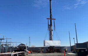 A Tesla Megapack being expertly suspended mid-air during the lifting process by Winslow Crane. Notably, two taglines were employed to ensure controlled and safe handling during this operation.