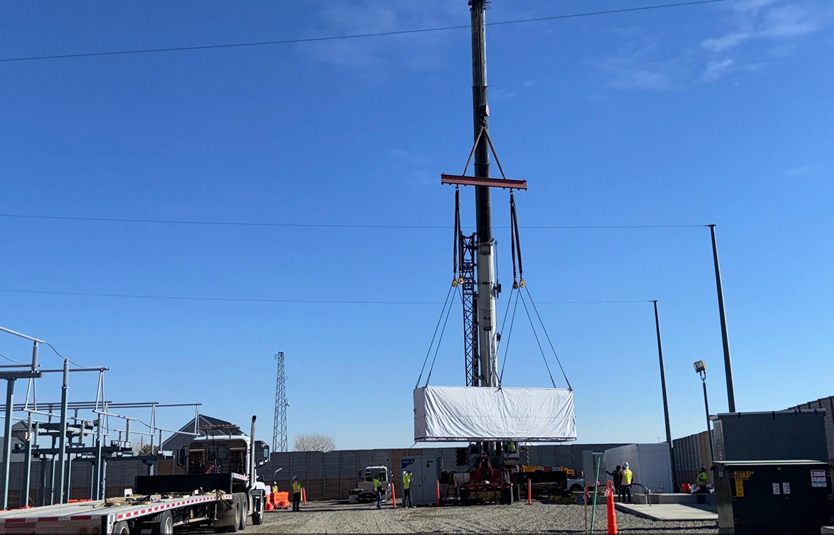 A Tesla Megapack being expertly suspended mid-air during the lifting process by Winslow Crane. Notably, two taglines were employed to ensure controlled and safe handling during this operation.