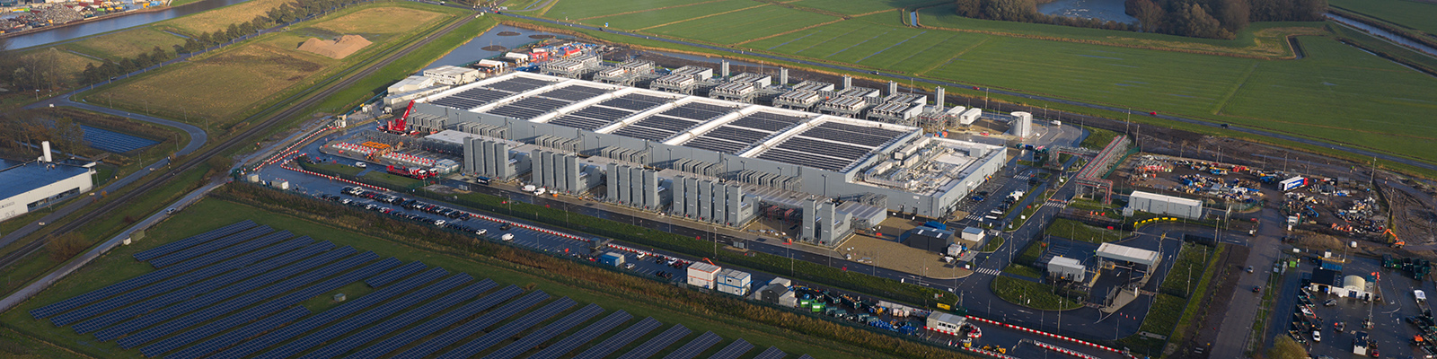 hero-image Large data center campus with ground mounted solar arrays powering sustainable cloud computing infrastructure in a green rural landscape, showcasing clean energy and tech growth.