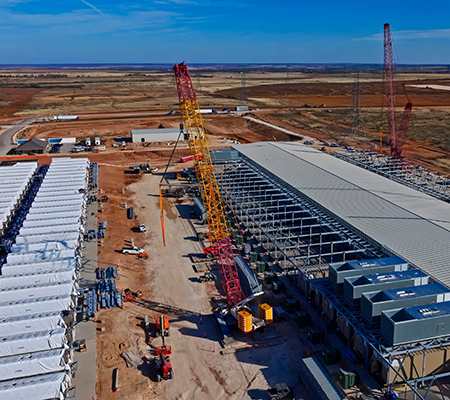 Aerial construction view shows data center structures BESS batteries red cranes and metal framing.