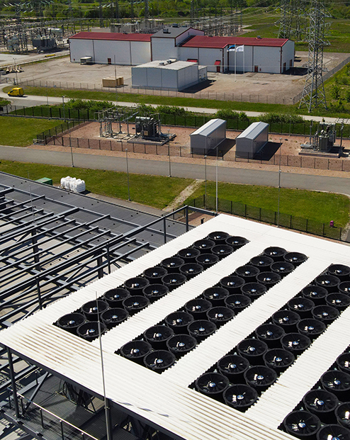 Aerial view of a data center rooftop with large cooling fans and adjacent electrical substation, highlighting power infrastructure, HVAC climate control, and industrial-scale operations.