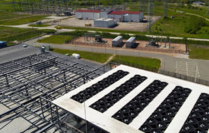 Aerial view of a data center rooftop with large cooling fans and adjacent electrical substation, highlighting power infrastructure, HVAC climate control, and industrial-scale operations.