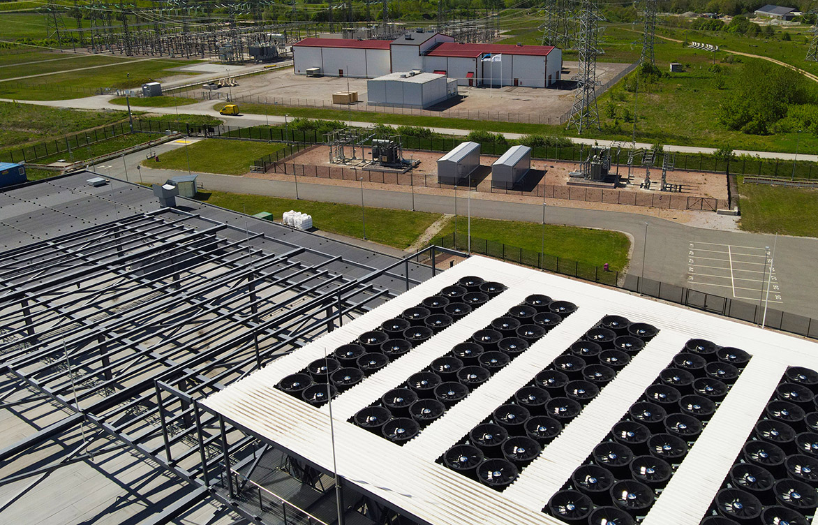 Aerial view of a data center rooftop with large cooling fans and adjacent electrical substation, highlighting power infrastructure, HVAC climate control, and industrial-scale operations.
