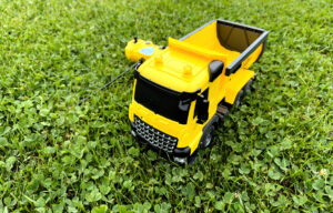 Overhead view of a radio-controlled play truck with a remote sitting next to it on the green lawn of a backyard.
