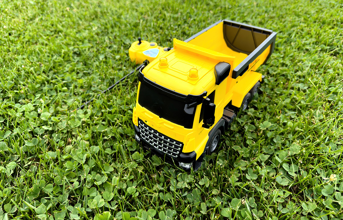 Overhead view of a radio-controlled play truck with a remote sitting next to it on the green lawn of a backyard.