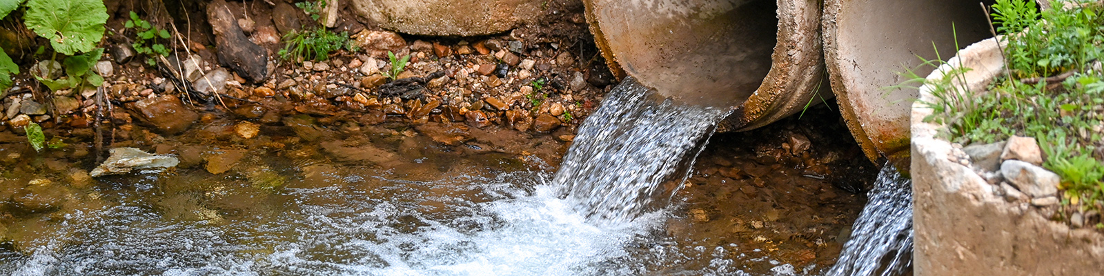 hero-image Wastewater discharge flows from pipes into a river.