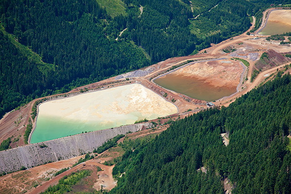 Aerial view of lined water containment ponds surrounded by forested mining operations.