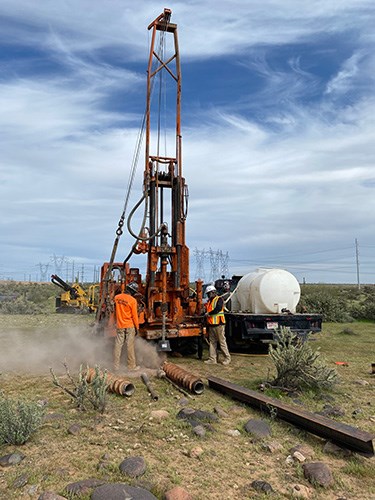 A drill rig drilling a test pile into desert soil under a clear sky.