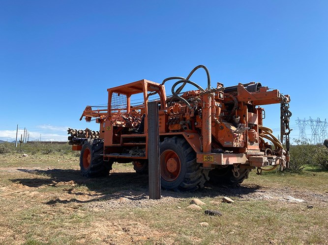 A drill rig parked next to a steel test pile in the desert.