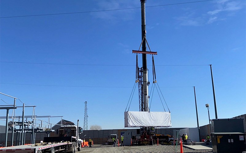 A crane lowering a Tesla Megapack battery to the ground at a substation in Colorado