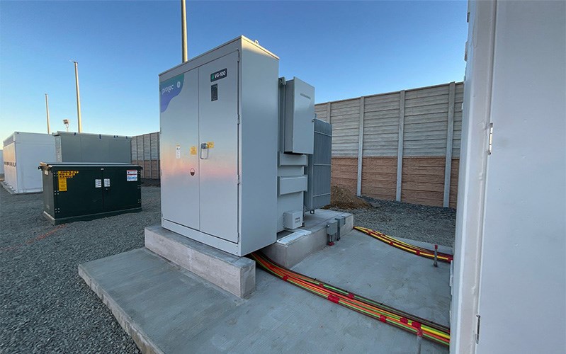 A transformer resting on a concrete foundation connected with transmission cables to a Tesla Megapack battery
