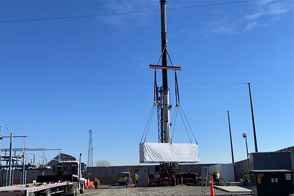 A crane lowering a Tesla Megapack battery to the ground at a substation