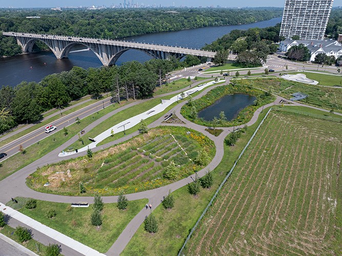 Aerial image of a rain garden and stormwater pond with an apartment building and a bridge crossing a large river in the background..