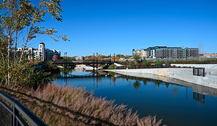A narrow, concrete-walled stormwater pond with trees and a bridge crossing in the background
