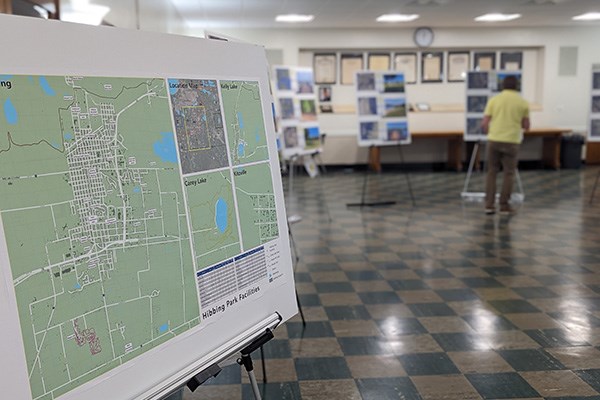 A poster-size map presented on an easel at a public meeting with a person examining other posters in the background.