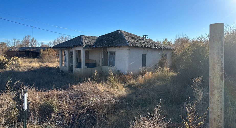 A dilapidated historic building in a desert-scrub landscape under a clear blue sky.