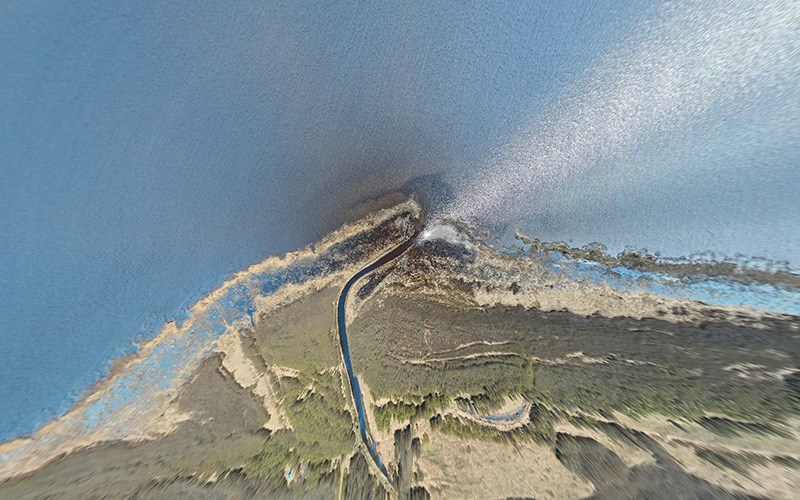 Aerial view of a river flowing into a lake, forming a small inlet with surrounding shoreline and vegetation.